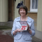 Woman in elegant dress holding a gift box outside Buckingham Palace.