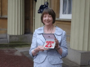Woman in elegant dress holding a gift box outside Buckingham Palace.