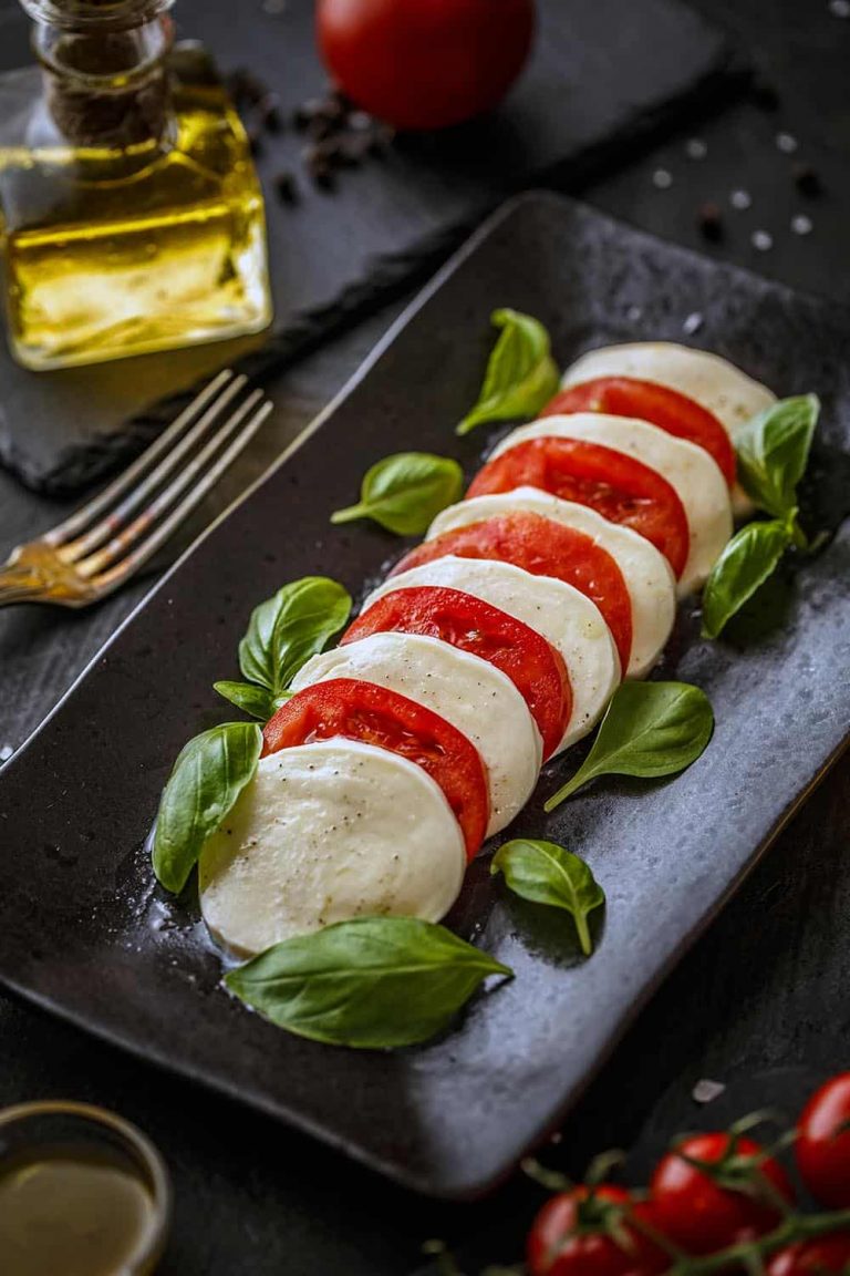 Caprese salad with mozzarella, tomato, and basil on black plate.