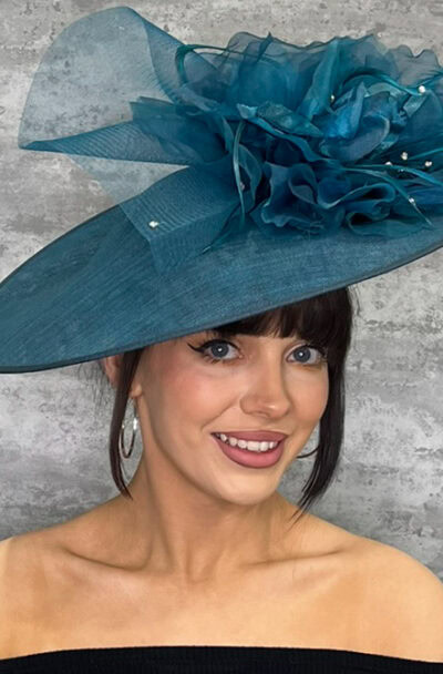 Elegant blue disc style hat with floral decoration and netting for special occasions.