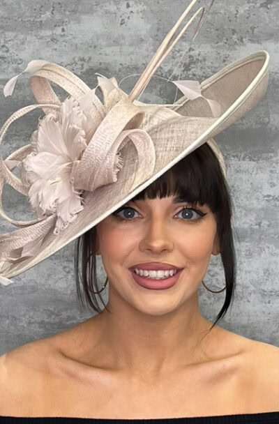 Woman wearing a large, elegant saucer style hat with floral and ribbon details.