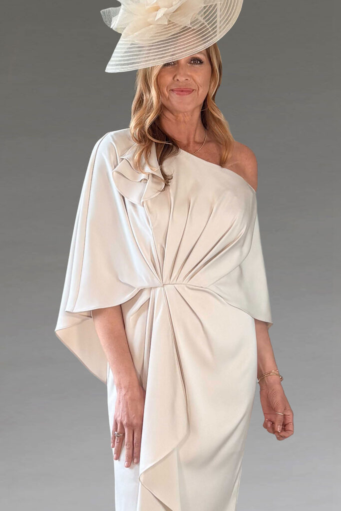 Woman in an elegant cream one-shoulder dress and hat.