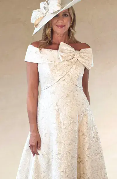 A smiling woman in an elegant cream dress and hat.