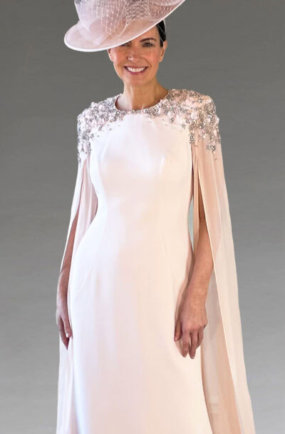 Woman in elegant blush pink caped dress with matching hat.