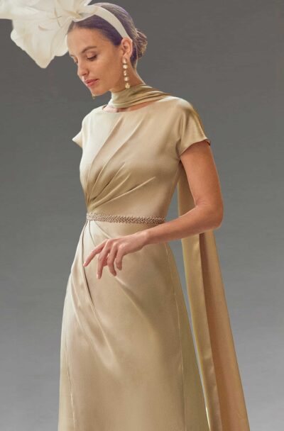 An elegant woman in a champagne gold dress and fascinator.