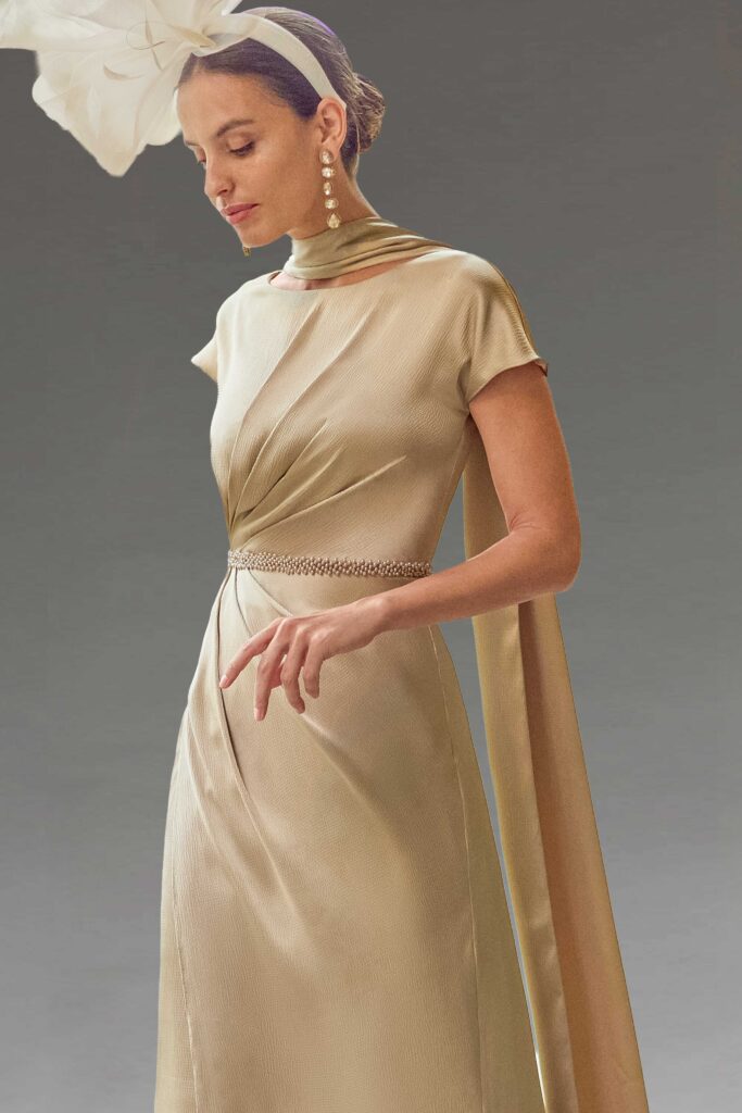 An elegant woman in a champagne gold dress and fascinator.