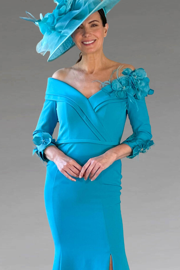A smiling woman in a turquoise off-the-shoulder dress and hat.