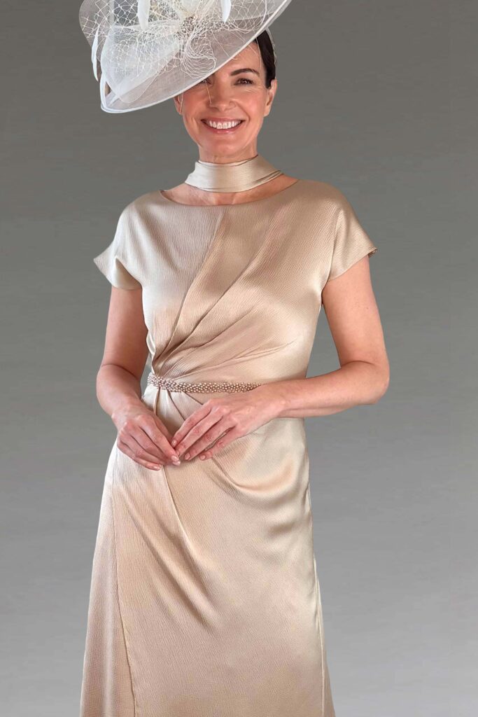 A smiling woman in a champagne dress and white fascinator.