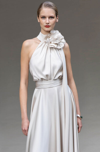 Model in an elegant cream halterneck dress with floral corsage.