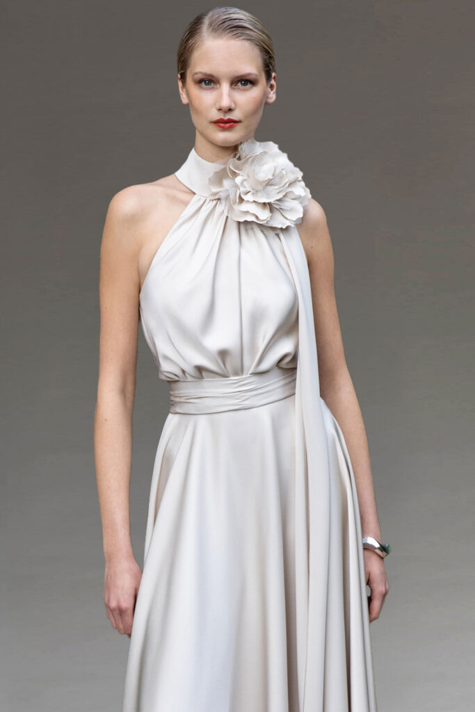 Model in an elegant cream halterneck dress with floral corsage.