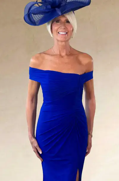 A smiling woman in a blue dress and matching fascinator.