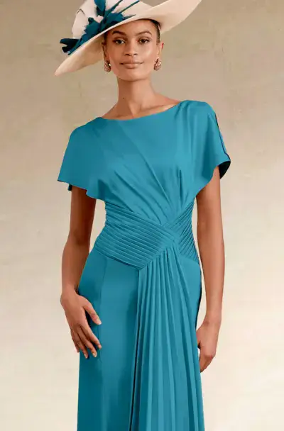 Woman in an elegant teal dress and cream fascinator hat.